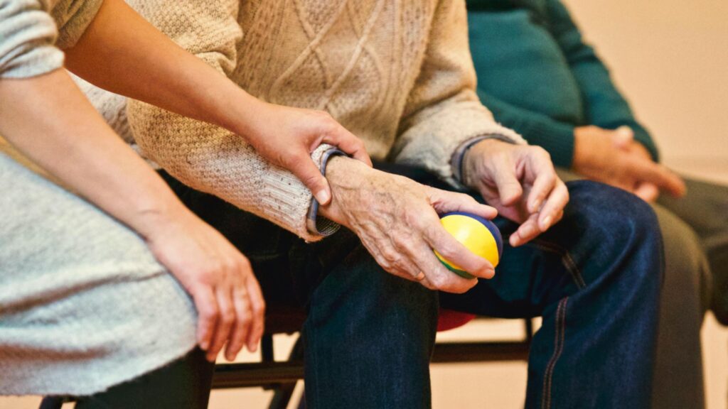 A nurse providing care to an elderly person holding a small juggling ball. Both people are seated.